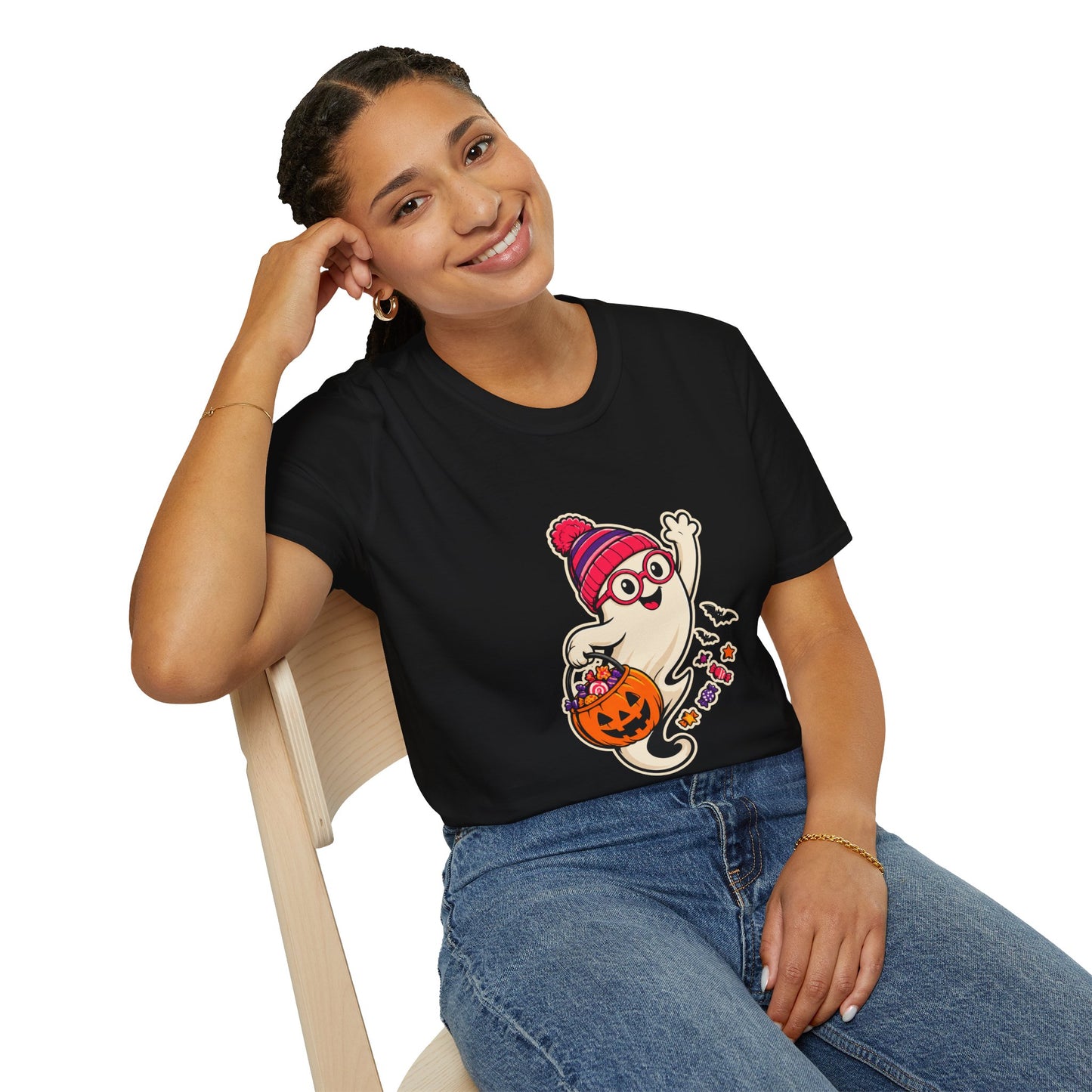 A black short-sleeve crewneck t-shirt featuring a cartoon graphic of a cute ghost wearing a pink and red striped knit hat and glasses, holding a jack-o'-lantern bucket filled with candy.