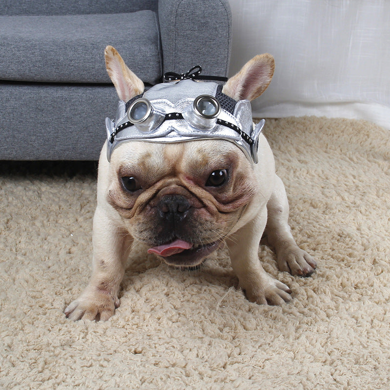 Dog wearing a silver helmet with goggles on a carpeted floor.