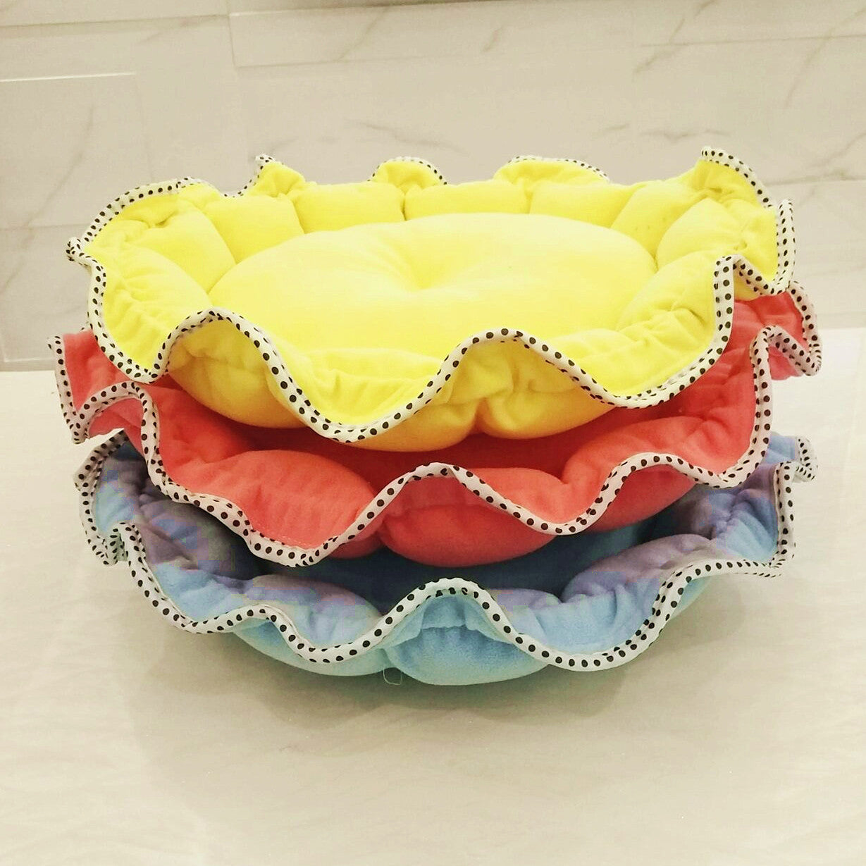 Stack of colorful pet beds with ruffled edges on a light background