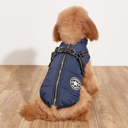 Small dog wearing a blue puffer vest with a brand logo on a wooden floor.