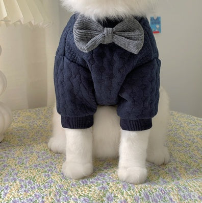 Dog wearing a navy blue knitted outfit with a gray bow tie on a floral-patterned surface.