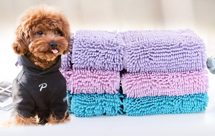 Small dog wearing a black outfit next to a stack of colorful textured towels.