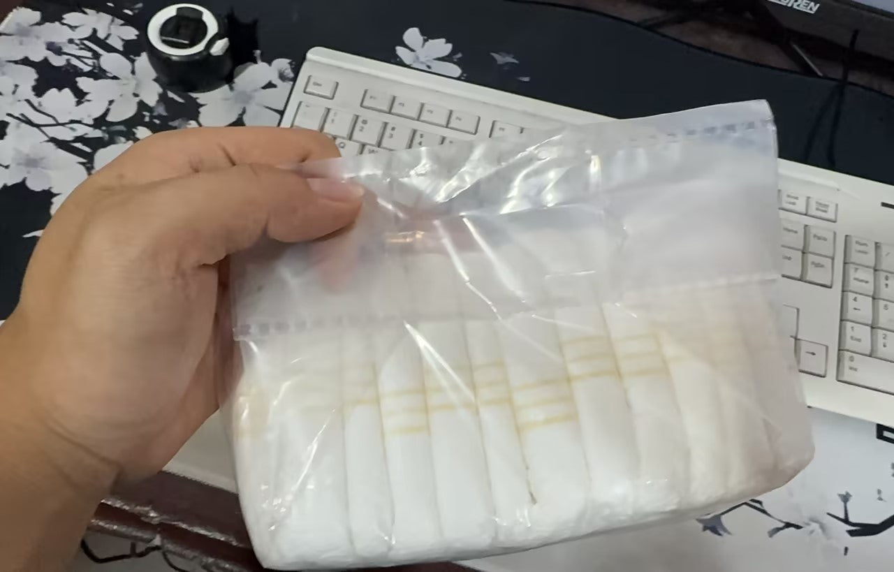 Hand holding a clear plastic bag with white items on a desk with a keyboard and mouse.