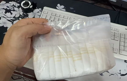 Hand holding a clear plastic bag with white items on a desk with a keyboard and mouse.