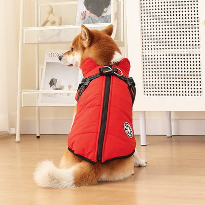 Dog wearing a red puffer vest indoors on a wooden floor.