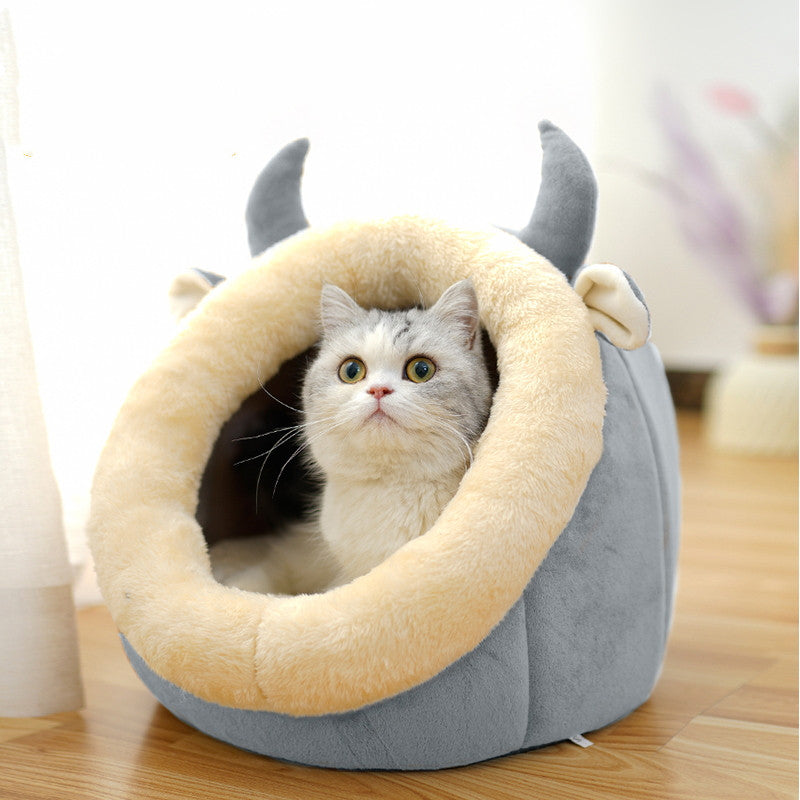 Cat lying inside a gray pet bed with animal-like horns on a wooden floor.