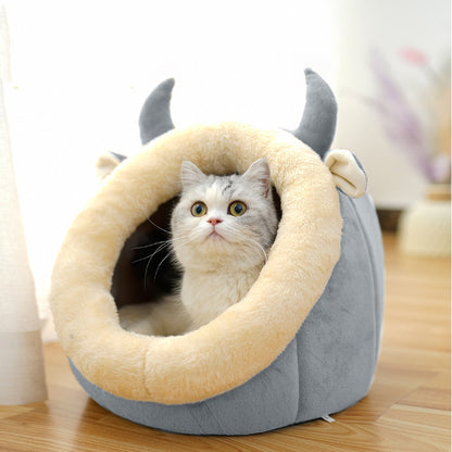 Cat lying inside a gray pet bed with animal-like horns on a wooden floor.