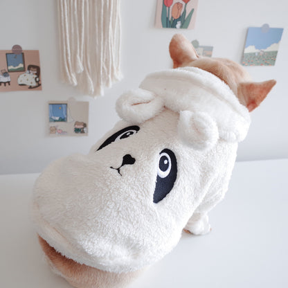 Dog wearing a white hood with cartoon face design on a light-colored surface.