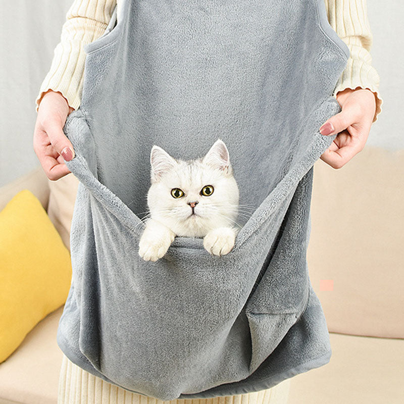 Person holding a gray pet sling with a white cat inside, sitting on a beige couch.