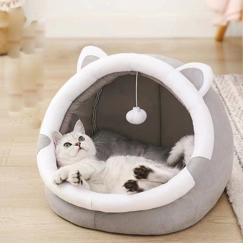 Cat lying in a gray and white pet bed with cat ears on a wooden floor.