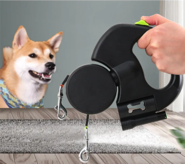 Black retractable dog leash with a hand holding it, next to a dog on a wooden floor.