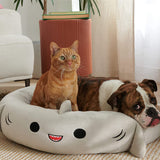 Cat and dog lying on a shark-shaped pet bed in a cozy living room.
